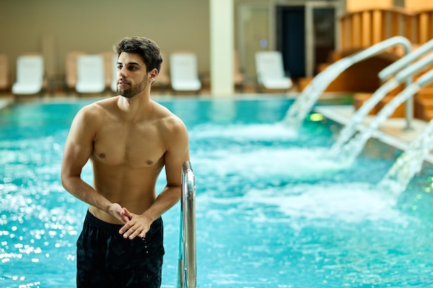 Homem de construção muscular jovem saindo da piscina enquanto passa um dia no spa