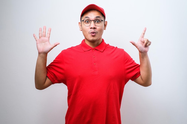 Homem de correio asiático vestindo uniforme de entrega e boné mostrando e apontando para cima com os dedos número dez enquanto sorri confiante