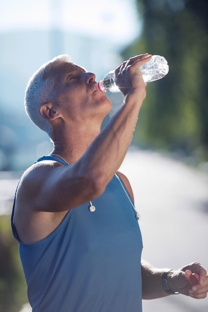 homem de corrida sênior bonito bebendo água fresca da garrafa após a corrida matinal