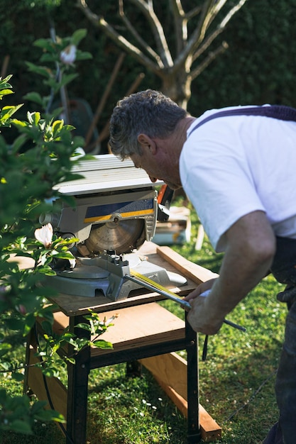 Homem de costas trabalhando madeira no jardim