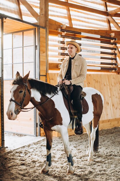 Homem de cowboy bonito andando a cavalo em um rancho