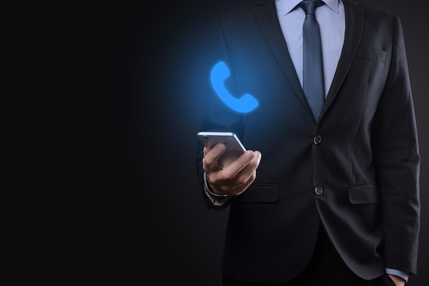 Homem de empresário de terno na parede preta segura o ícone do telefone. Ligue agora para o conceito de tecnologia de serviço ao cliente do centro de suporte de comunicação empresarial.
