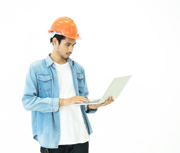 Homem de engenheiro arquiteto asiático jovem inteligente usar jeans casual e capacete de segurança laranja que mão segurando o laptop para verificar seu plano de trabalho com posição séria e pensando