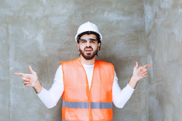 Homem de engenheiro com capacete branco e óculos de proteção, apontando para algo.