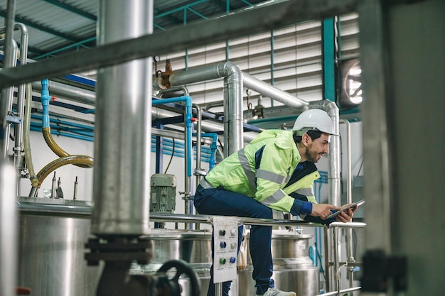 Homem de engenheiro técnico caucasiano de uniforme com tablet verificando e controlando tanques de caldeira e encanamento líquido na linha de produção da fábrica química