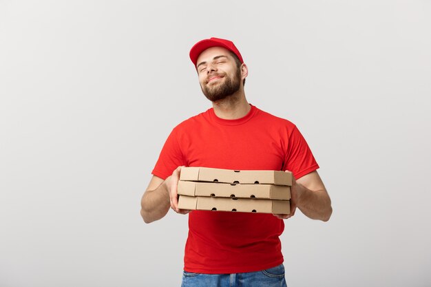 Homem de entrega bonito da pizza que mostra a expressão deliciosa sobre o fundo cinzento