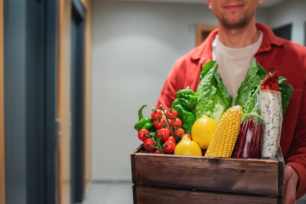 Foto homem de entrega segurando saco de papel com comida na entrada o mensageiro dá a caixa com legumes e frutas frescas ao cliente