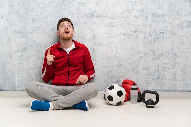 Homem de esporte ruiva apontando para cima e surpreso