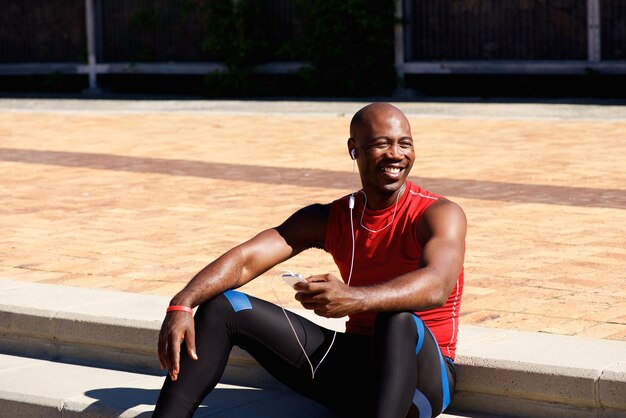 Homem de esportes africano sentado ao ar livre e ouvir música