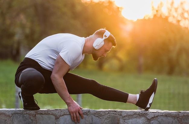 Homem de esportes em forma ouvindo música enquanto faz exercícios de alongamento antes de correr ou malhar ao ar livre