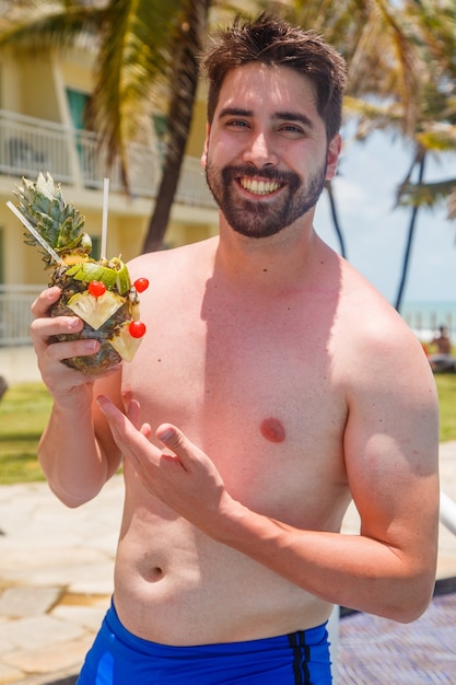 Homem de férias em risort, bebendo uma bebida doce de abacaxi.