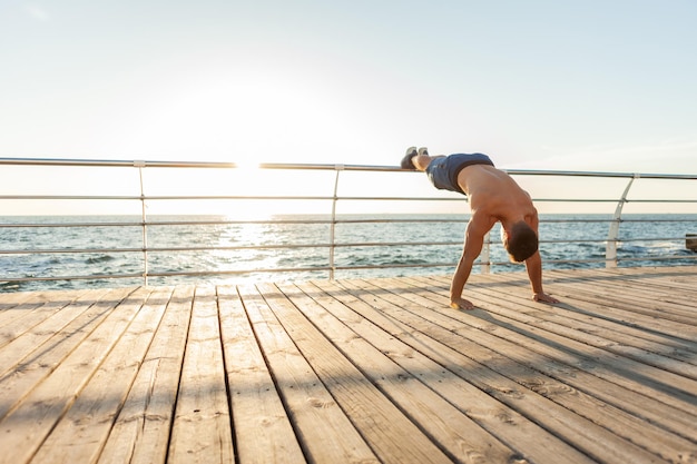 Homem de fitness bonito musculoso com torso nu fazendo flexões na praia ao nascer do sol