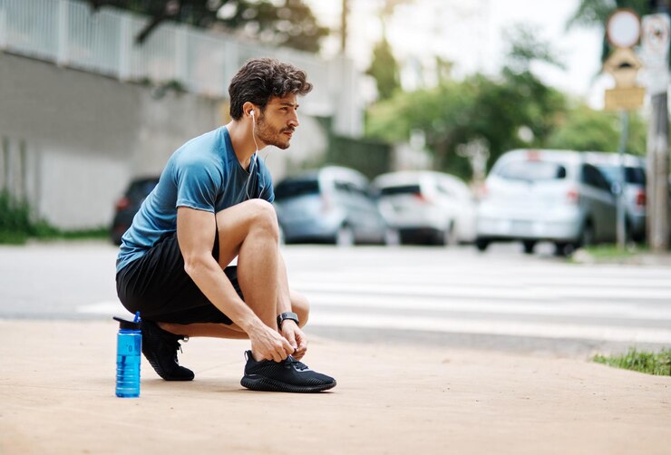 Foto homem de fitness e amarrar atacadores na rua exercício e treino ou preparação de segurança com rotina matinal fones de ouvido tecnologia de áudio e streaming motivação ou música corredor e atleta fora