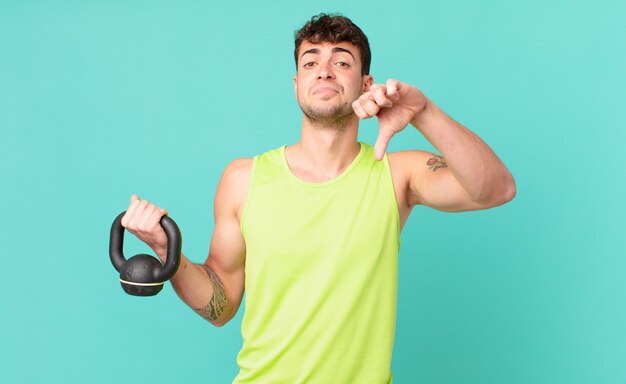 Homem de fitness sentindo-se zangado, irritado, irritado, desapontado ou insatisfeito, mostrando o polegar para baixo com um olhar sério