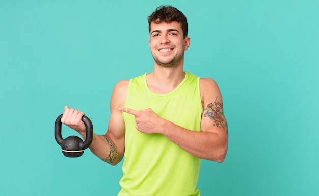 Homem de fitness sorrindo alegremente, sentindo-se feliz e apontando para o lado e para cima, mostrando o objeto no espaço da cópia