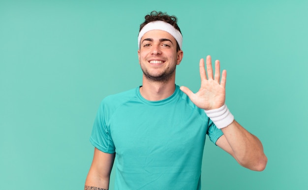 Homem de fitness sorrindo e parecendo amigável, mostrando o número cinco ou quinto com a mão para a frente, em contagem regressiva