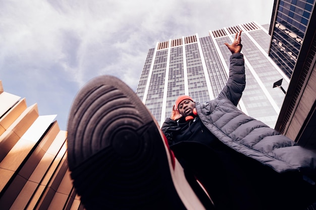 Homem de hip-hop andando acima da lente da câmera sob arranha-céus elegante dj afro-americano se apresentando na rua