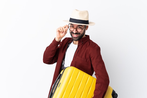 Homem de homem viajante com barba segurando uma mala sobre branco com óculos e sorrindo