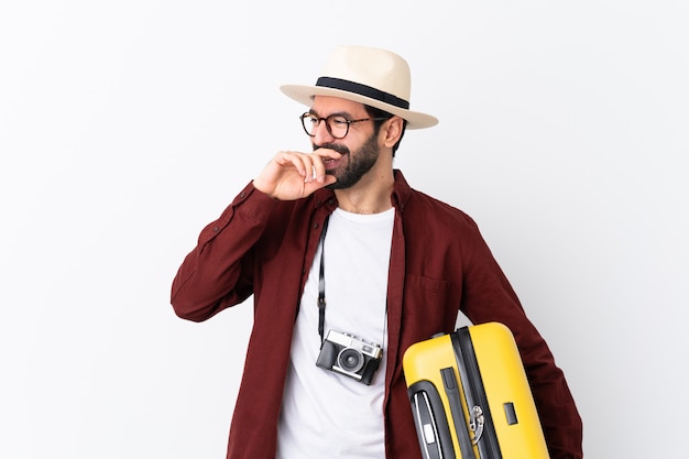 Homem de homem viajante com barba segurando uma mala sobre branco sorrindo muito