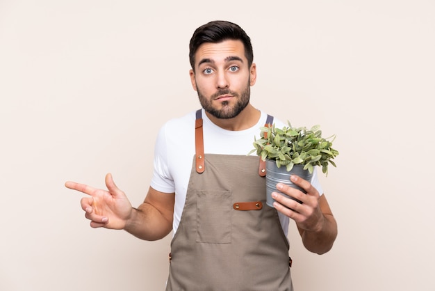 Homem de jardineiro segurando uma planta mais apontando para as laterais tendo dúvidas