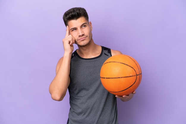 Homem de jogador de basquete jovem caucasiano isolado em fundo roxo com dúvidas e pensando