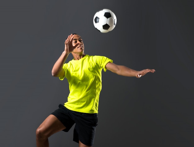 Homem de jogador de futebol com pele escura jogando batendo a cabeça no fundo escuro