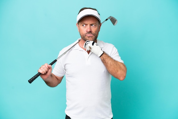 Foto homem de jogador de golfe caucasiano de meia-idade isolado em fundo azul com dúvidas e pensando