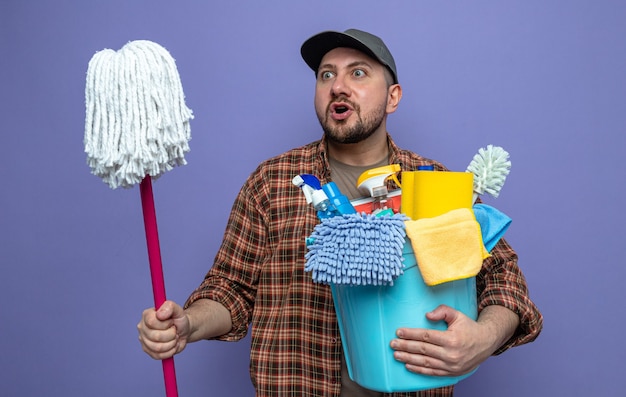 Homem de limpeza eslavo surpreso segurando equipamento de limpeza e esfregão