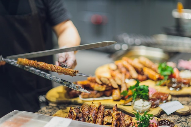 Homem de luvas pretas coloca cordeiro com espátula para comida no prato branco Carne marrom cozida saborosa de cordeiro