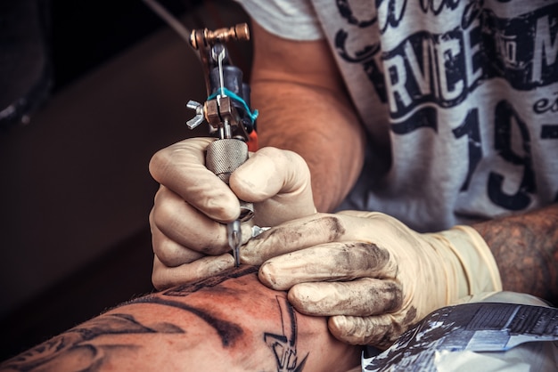 Homem de luvas trabalha em estúdio de tatuagem.