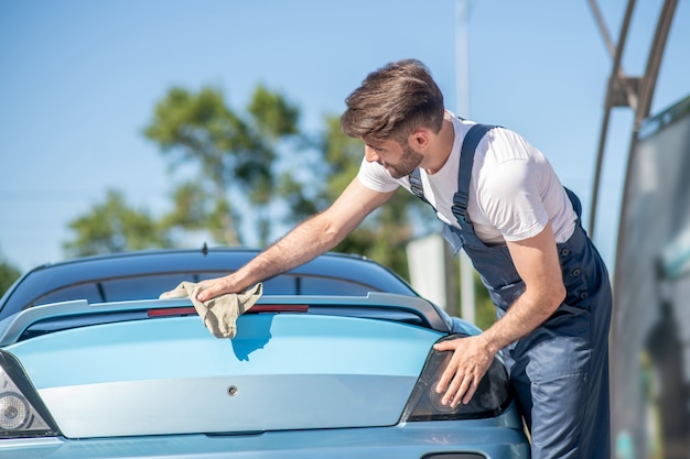 Homem de macacão, limpando completamente o carro