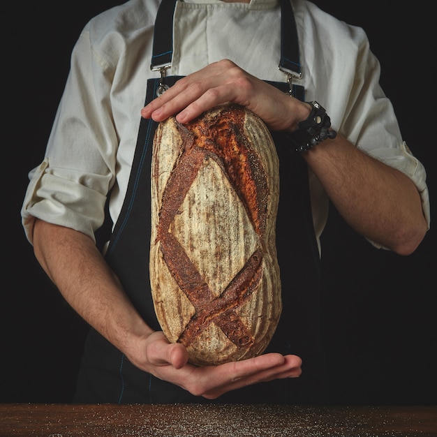 homem de mãos segurando um pão caseiro escuro fresco