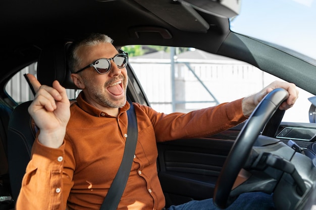 Homem de meia-idade alegre em roupa casual desfrutando de uma viagem de carro sozinho ouvindo música cantando músicas
