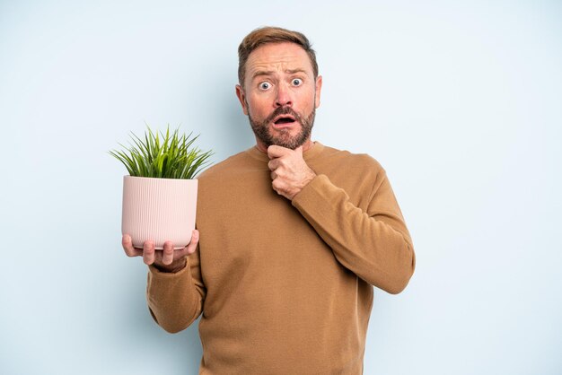 Homem de meia idade com boca e olhos bem abertos e mão no queixo. conceito de vaso de planta