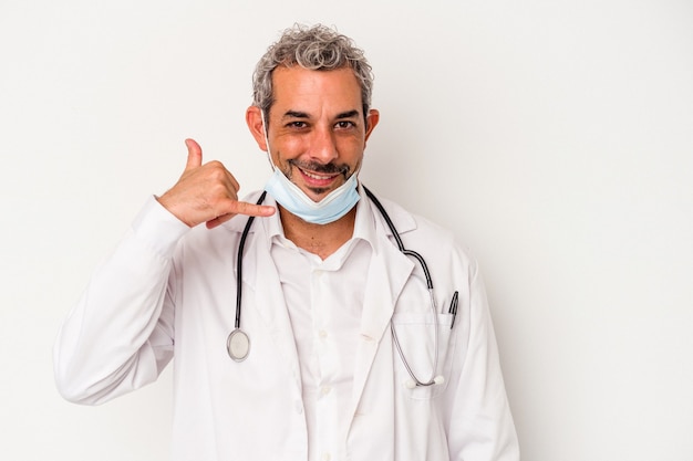 Homem de meia idade médico usando uma máscara para vírus isolado no fundo branco, mostrando um gesto de chamada de telefone móvel com os dedos.