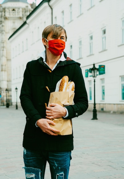 Foto homem de meia idade na rua com pão, baguete, compras de pão durante a pandemia global, usando máscara, obtendo pão na padaria. comida para viagem e compras de padaria durante o dia 19.