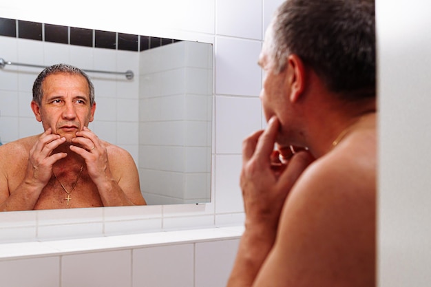 Homem de meia idade olhando no espelho no banheiro
