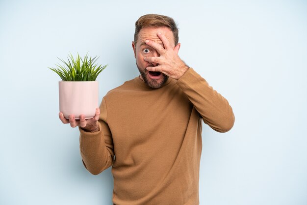 Homem de meia idade parecendo chocado, assustado ou apavorado, cobrindo o rosto com a mão. conceito de vaso de planta