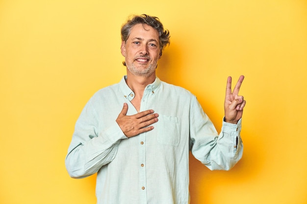 Homem de meia-idade posando em um pano de fundo amarelo fazendo um juramento colocando a mão no peito