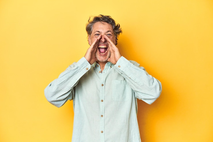 Foto homem de meia idade posando em um pano de fundo amarelo gritando animado para a frente