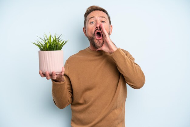 Homem de meia idade se sentindo feliz, dando um grande grito com as mãos ao lado da boca. conceito de vaso de plantas