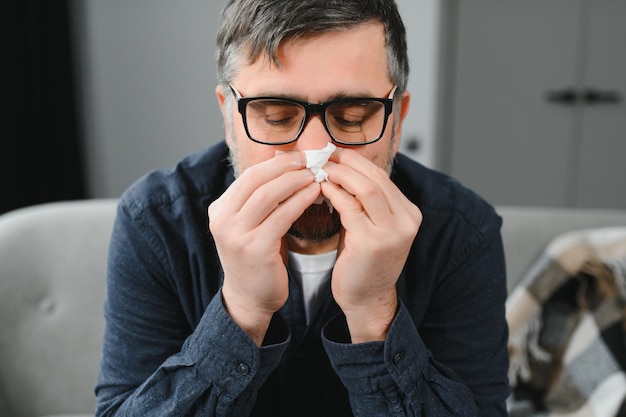 Homem de meia-idade se sentindo mal com resfriado e febre em casa doente com gripe sentado no sofá