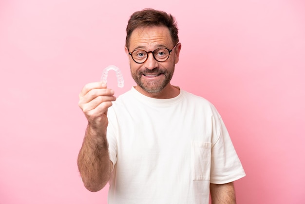 Homem de meia idade segurando aparelho invisível isolado no fundo rosa com expressão feliz