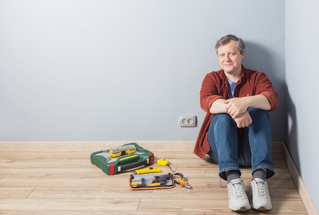 Homem de meia-idade sentado no chão ao lado de uma caixa de ferramentas de conserto