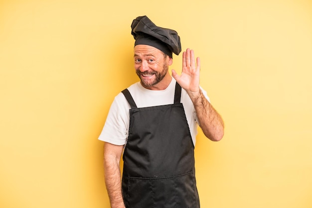 Homem de meia idade sorrindo alegremente, acenando com a mão, dando as boas-vindas e cumprimentando você. conceito de chef