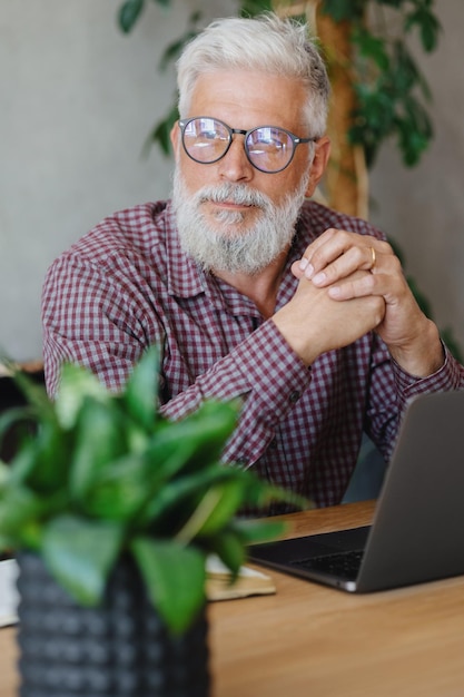 Homem de negócios adulto com cabelos grisalhos está trabalhando em um laptop em sua carreira de escritório, finanças e marketing