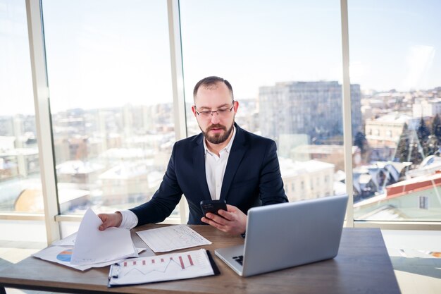 Homem de negócios adulto de sucesso, professor e mentor está trabalhando em um novo projeto. Senta-se à mesa perto da grande janela. Funciona em um laptop