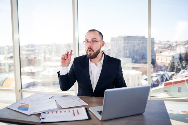 Homem de negócios adulto de sucesso, professor e mentor está trabalhando em um novo projeto. Senta-se à mesa perto da grande janela. Funciona em um laptop