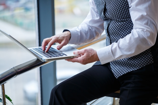 Homem de negócios adulto, professor, mentor trabalhando em um novo projeto. Senta-se junto a uma grande janela sobre a mesa. Ele olha para a tela do laptop.