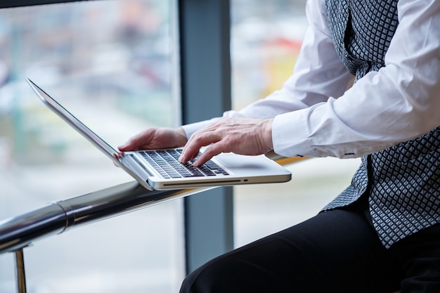 Homem de negócios adulto, professor, mentor trabalhando em um novo projeto. Senta-se junto a uma grande janela sobre a mesa. Ele olha para a tela do laptop.